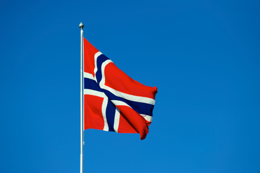 Flag of the Kingdom of Norway against blue sky on windy day in spring