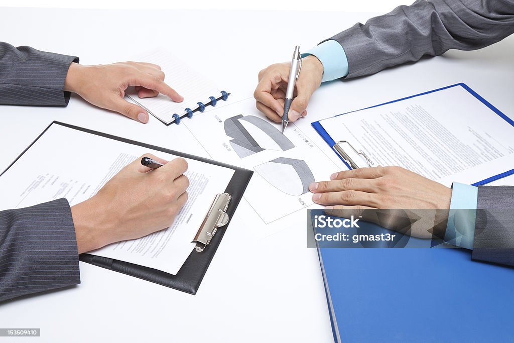 Businesspeople working together Two business people in elegant suits sitting at desk working in team together with documents sign up contract, holding clipboard, folder with papers, business plan. Isolated over white background. Adult Stock Photo