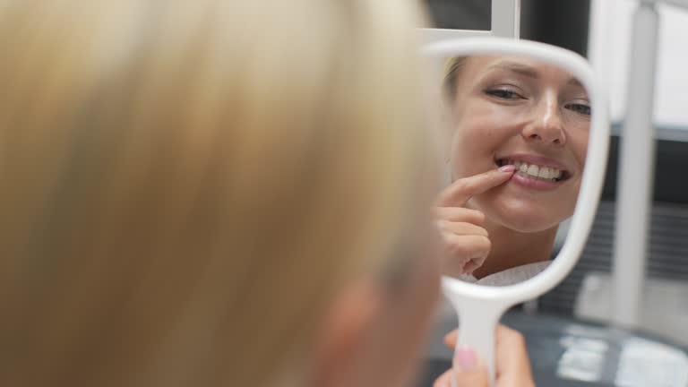 Closeup back view of blonde cheerful young woman patient smiling into mirror looking at healthy white teeth enjoying dental healthcare facilities.