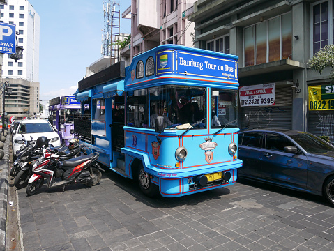 July 11, 2023 - Bandung, West Java, Indonesia.\nA blue coloured Bandung Tour on Bus or Bandung Bandros sightseeing bus full of tourists on Jl. Braga in downtown Bandung City, used to get around the city.