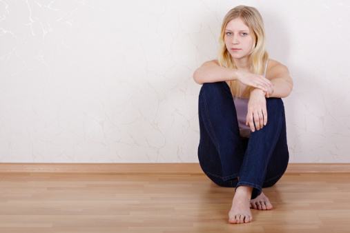 Young girl sits calmly and with back pressed against wall.