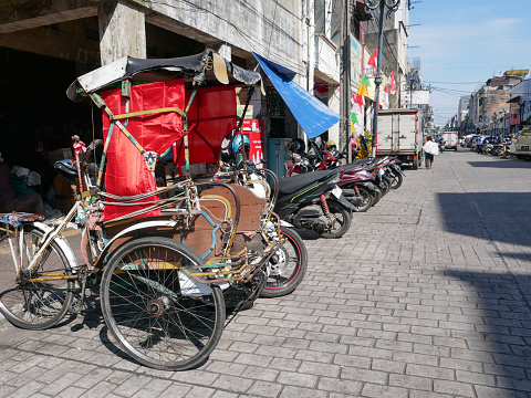 May 17, 2023 - Bandung, West Java, Indonesia.
A view of a parked becak on the side of Jl. Cibadak in downtown Bandung City with a paved road. Becak's are common in Bandung and are one of the cheapest ways of getting around the city. Jl. Cibadak is famous for wholesale shops.