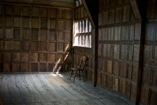 A wooden chair sitting under a window in an english 15th century wooden panelled room.