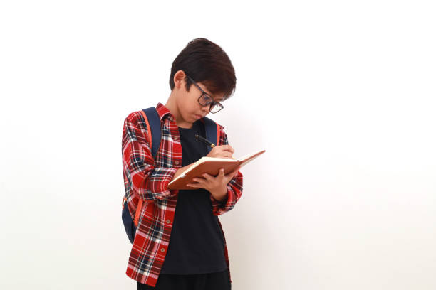 istock Portrait of asian student standing while writing something on a book. Isolated on white 1535242855