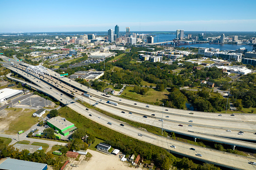 Aerial view of Jacksonville city with high office buildings and american freeway intersection with fast moving cars and trucks. USA transportation infrastructure concept.