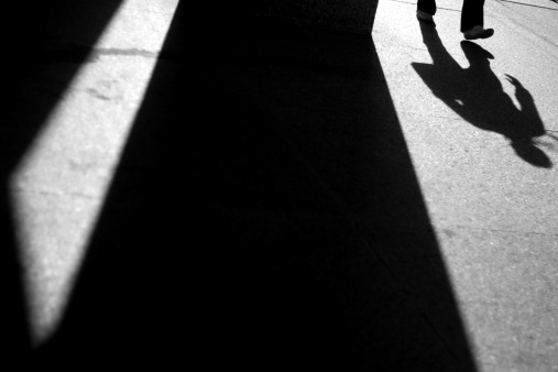 black and white landscape image showing long shadows of man walking and buildings. picture leaves room for text or logo.
