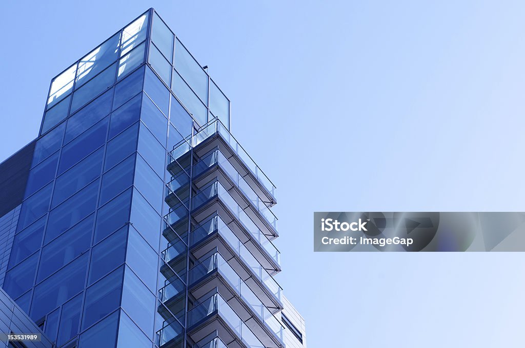 High Rise Living Modern glass residential building with balconies and clear sky backdrop Blue Glass Stock Photo