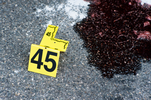 Evidence marker with measuring gauge on pavement next to red liquid (blood, vehicle fluid)