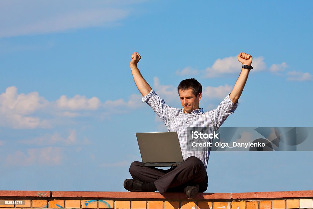 Businessman Sits and Celebrates with Laptop Outdoors Young happy man working outside with his laptop and celebrates with his arms in the air Achievement Stock Photo