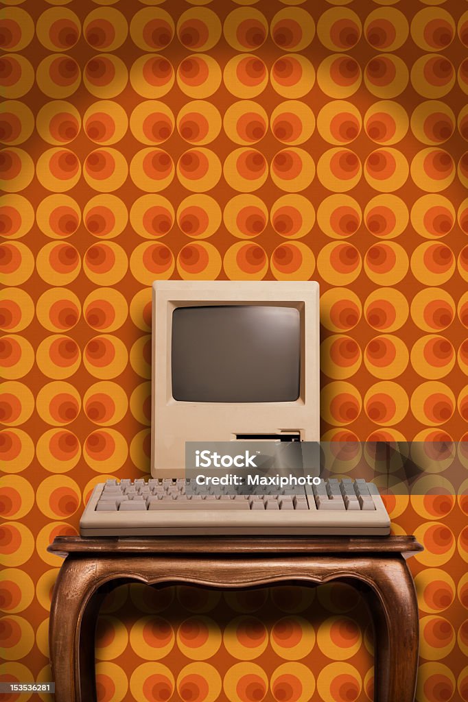 Old desktop computer on wooden table and seventies wallpaper An old classic computer from the eighties against a colourful wallpaper from the seventies, with plenty of copy space for editing. Computer Stock Photo