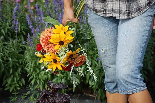 Woman with denim jeans holding a colorful bouquet of flowers.