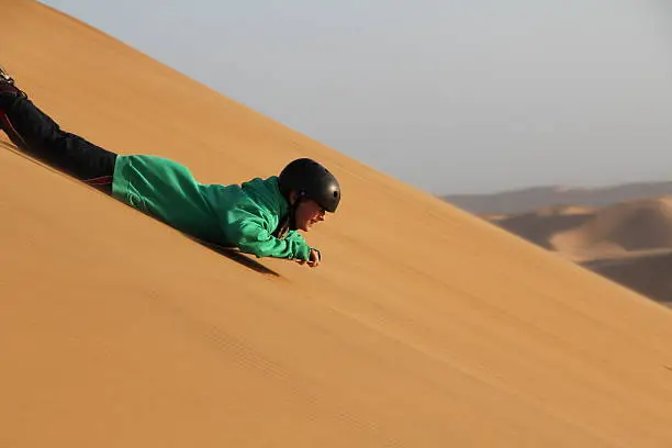 Young boy sand- sledding  on the dunes in Namibia