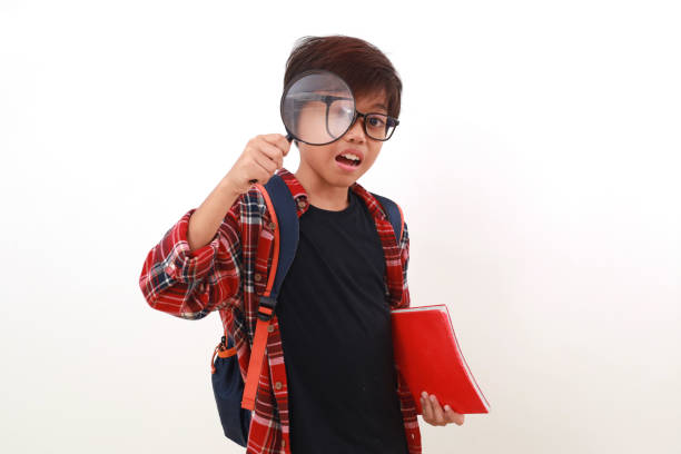 Happy smart asian student holding a book while looking through a magnifying glass. Isolated on white