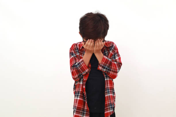 Stressed asian boy standing while covering his face. Isolated on white