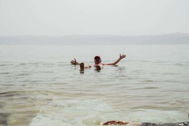 An Asian tourist traveler floating in the therapeutic water of the dead sea, placed in border of Israel and Jordan