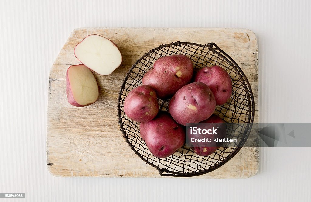 Rojo papas en cesta de alambre en la tabla de cortar. - Foto de stock de Patata roja libre de derechos