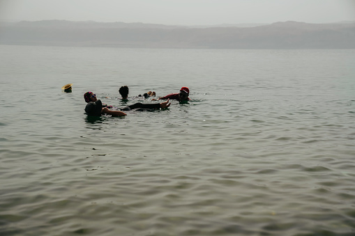 An Asian tourist traveler floating in the therapeutic water of the dead sea, placed in border of Israel and Jordan