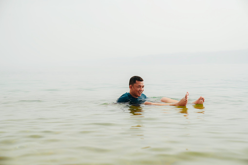 An Asian tourist traveler floating in the therapeutic water of the dead sea, placed in border of Israel and Jordan