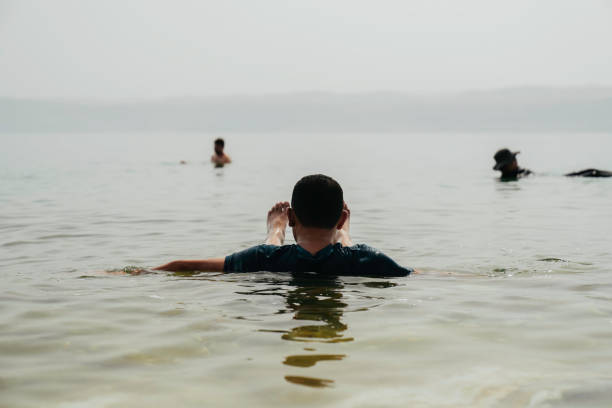 An Asian tourist traveler floating in the therapeutic water of the dead sea, placed in border of Israel and Jordan