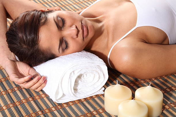 Beautiful young woman in a spa lying on a bamboo mat. Model wearing white vest, has head resting on white towel and eyes closed.
