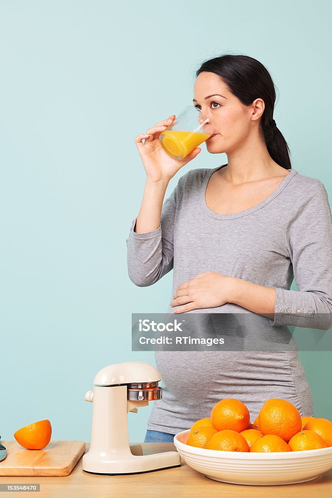 Pregnant woman making fresh orange juice. Photo of a 32 week pregnant woman in her kitchen drinking freshly squeezed orange juice. Orange Juice Stock Photo