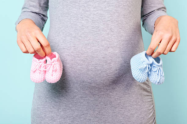 Pregnant woman holding pink and blue baby booties Photo of a woman who is 32 weeks pregnant holding baby booties, pink for a girl and blue for a boy. twin stock pictures, royalty-free photos & images