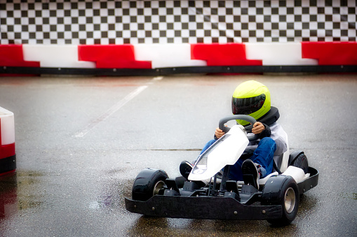 Children's karting competitions, the little racer smoothly passes the turn on the track. Teenage boy driving a go-kart learns to drive a car with a helmet on his head