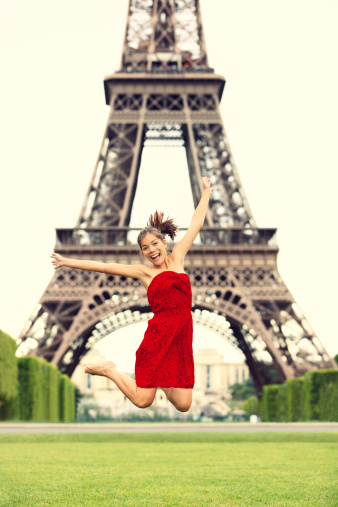 Paris girl at Eiffel Tower jumping happy smiling excited in red summer dress. Joyful young woman on Champs cheerful during vacation / holidays in Paris, France, Europe