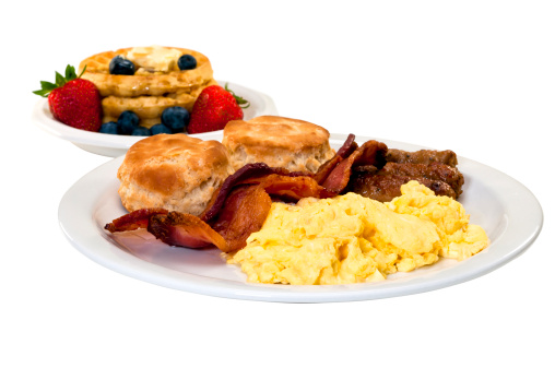Scrambled eggs, bacon, link sausage, biscuits,  and waffles with strawberries and blueberries.  Isolated on white background with clipping path.