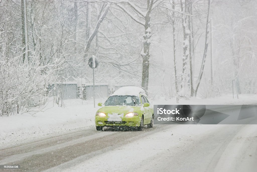 Traffic On A Winter Day Green car with headlamps driving with bad weather conditions: road is covered by snow. Blizzard Stock Photo