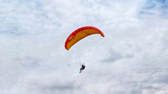 paragliding pilot with red orange parachute flying in the blue sky with white clouds