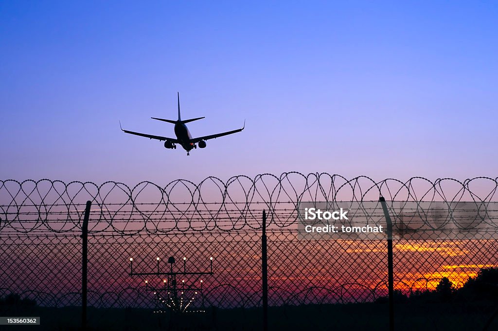 Jet airplane in the distance landing at sunset behind fence Jet airplane landing at sunset from Barcelona Airport Stock Photo