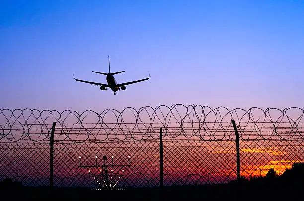 Photo of Jet airplane in the distance landing at sunset behind fence