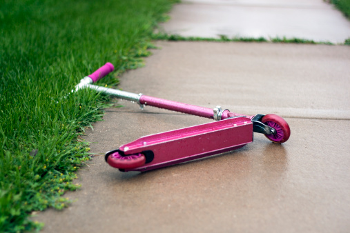 A pink scooter laying down in the rain.  There is a Sharp Depth of Field in Effect.
