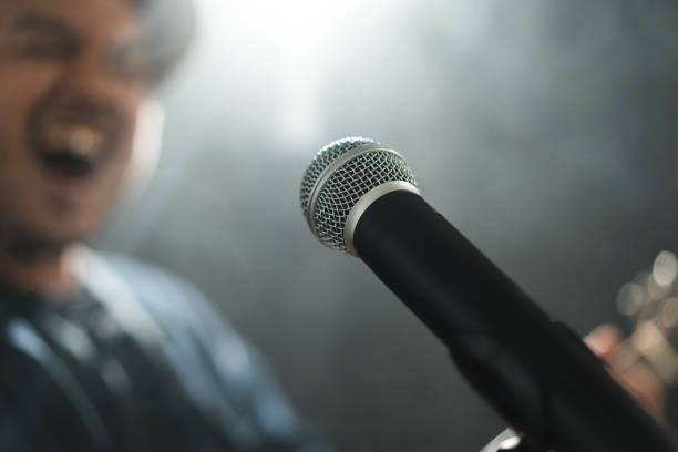 istock Attractive singer man singing music and playing guitar on stage with spotlight strike through the darkness at concert event. Musician performing live with light and smoke at hall. 1535620800