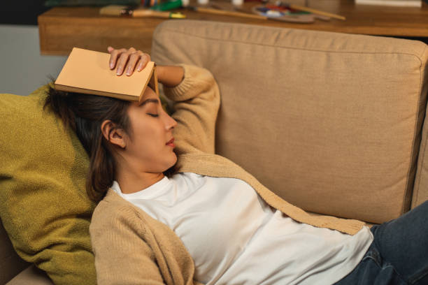 Sleeping Asian beautiful woman lay down on cozey couch sofa while reading book in living room with warm light at night. People female reading book until fall asleep stay home part time relax at home la hermosa mujer asiática dormida se acostó en el acogedor sofá del sofá mientras leía un libro en la sala de estar con luz cálida por la noche. las personas que leen libros hasta que se duermen se quedan en casa a tiempo parcial se relajan en casa