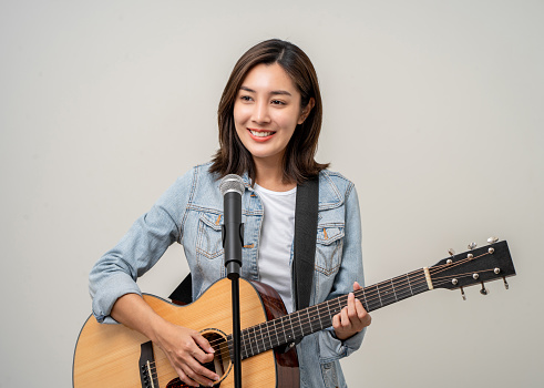 Happiness young asian woman singing song with guitar. Artist vocalist singer on isolated background. Confident woman public speaking talking with microphone in studio.