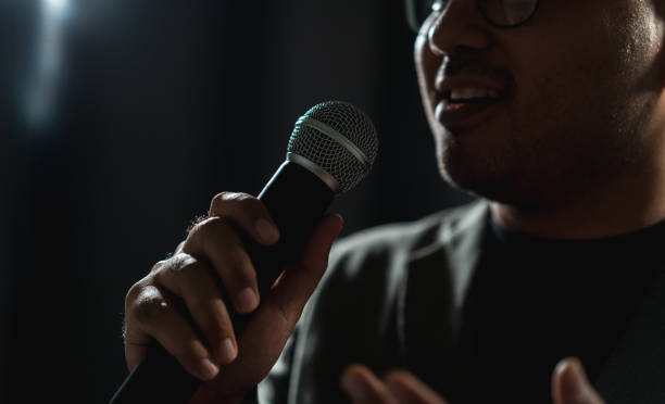 istock Confident successful speaker man talking on stage with spotlight strike through the darkness at corporate business event. Public speaker giving talk at conference hall. Stand up comedian. 1535648483