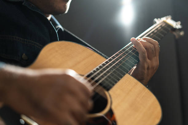 istock Attractive singer man singing music and playing guitar on stage with spotlight strike through the darkness at concert event. Musician performing live with light and smoke at hall. 1535648486