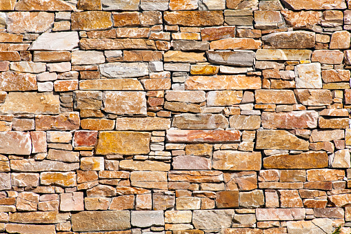 Stone wall made of irregular shaped natural rocks. The colors are gray and brown. Masonry. Background and texture