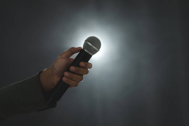 istock Confident successful speaker man talking on stage with spotlight strike through the darkness at corporate business event. Public speaker giving talk at conference hall. Stand up comedian. 1535652590