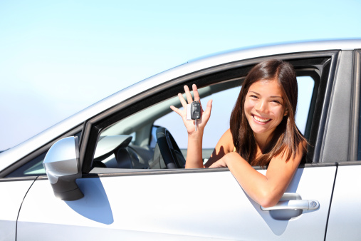 Asian car driver xwoman smiling showing new car keys and car. Mixed-race Asian and Caucasian girl.