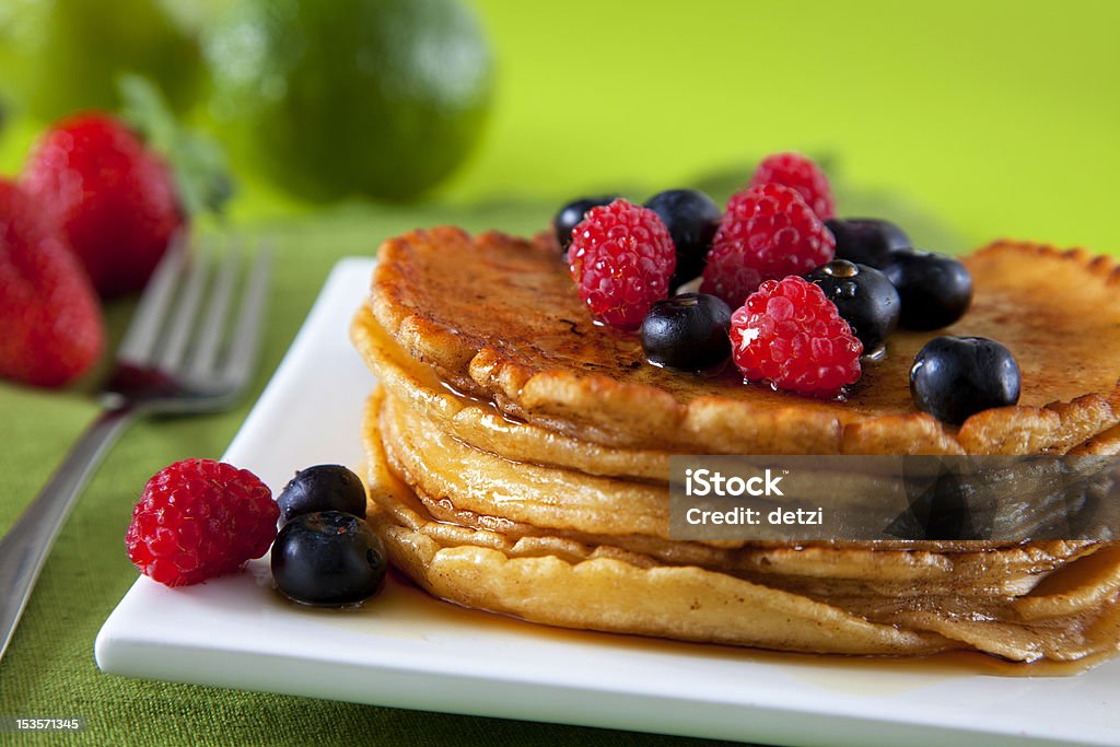 Pancakes with blueberries and raspberries Pancakes on a white plate with blueberries and raspberries in front of a green background. Black Color Stock Photo