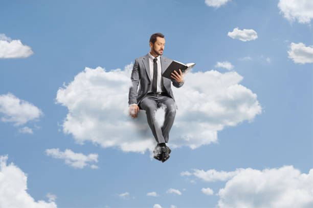 istock Professional man in a grey suit sitting on a cloud and reading a book 1535719137