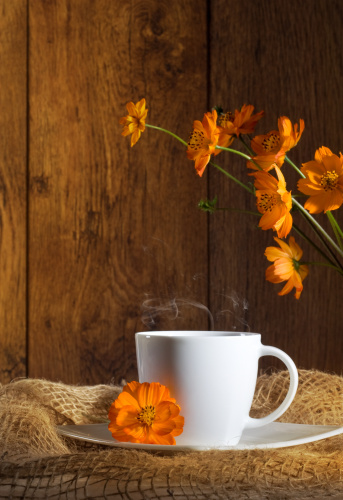 Cup of coffee with orange flowers on wooden background