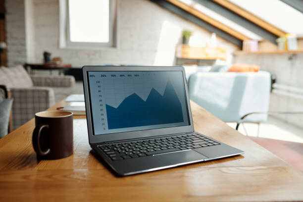 istock Laptop with blue financial graph on screen and brown mug standing on table 1535733357