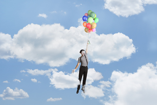 Mime flying and holding a bunch of balloons up in the blue sky