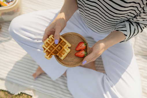 Cropped shot of woman holding waffles and strawberries on wooden plate