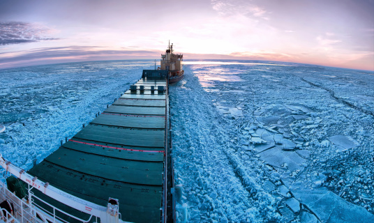 Icebreaker towing cargo ship through thick ice-field. Panoramic image made from 8 photos.