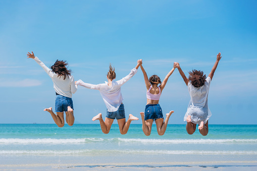 Happy childrens jumping on sand at beach. Teens playing and enjoying with friends at the sea. Vacations time and friendship concept.